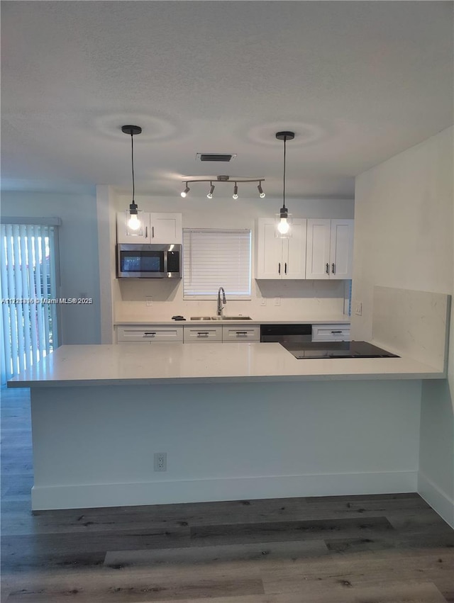 kitchen with kitchen peninsula, white cabinetry, hanging light fixtures, and sink