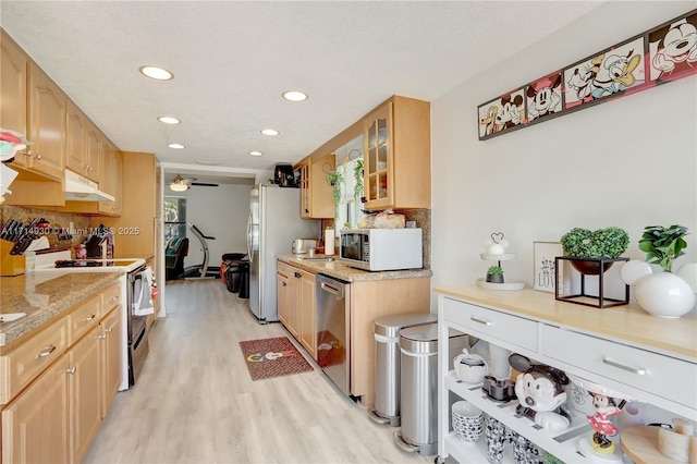 kitchen with light brown cabinetry, backsplash, stainless steel appliances, ceiling fan, and light hardwood / wood-style flooring