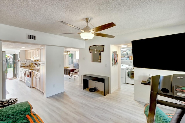 living room with washing machine and dryer, ceiling fan, a textured ceiling, and light wood-type flooring