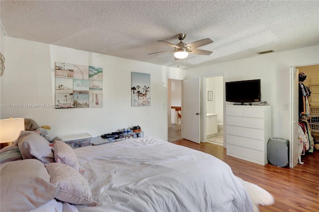 bedroom featuring a walk in closet, ensuite bathroom, ceiling fan, hardwood / wood-style flooring, and a closet