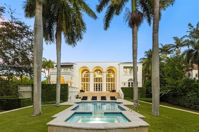 rear view of house with an in ground hot tub, a yard, and a balcony