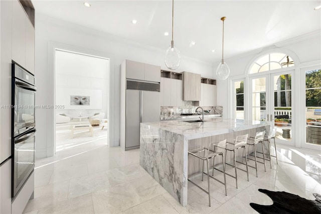 kitchen featuring a kitchen island with sink, sink, hanging light fixtures, light stone counters, and a breakfast bar area