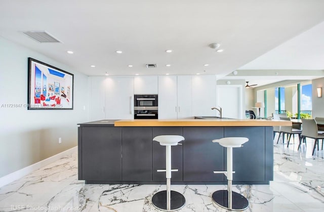 kitchen featuring white cabinetry, a large island, sink, butcher block countertops, and a breakfast bar area