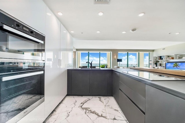 kitchen with electric stovetop, sink, white cabinets, and multiple ovens