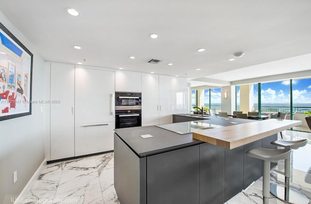 kitchen featuring black electric stovetop, a spacious island, sink, white cabinets, and a breakfast bar area