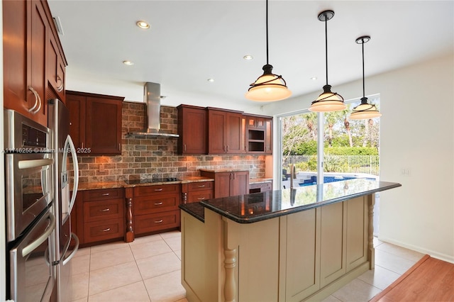 kitchen featuring light tile patterned flooring, appliances with stainless steel finishes, a kitchen island, dark stone counters, and wall chimney exhaust hood