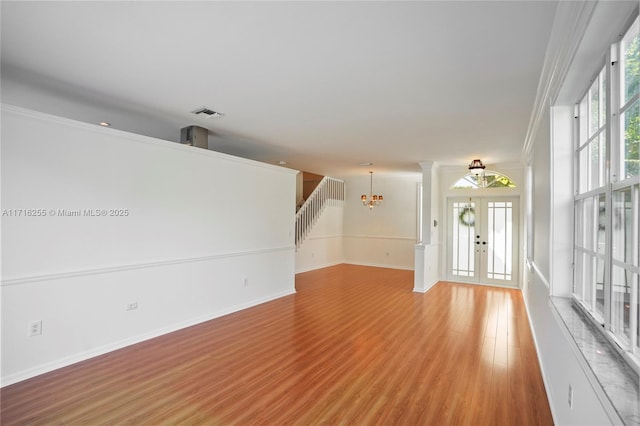 unfurnished living room featuring a notable chandelier, hardwood / wood-style floors, french doors, and a healthy amount of sunlight