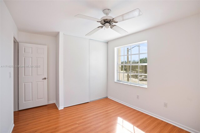 unfurnished bedroom with multiple windows, light wood-type flooring, ceiling fan, and a closet