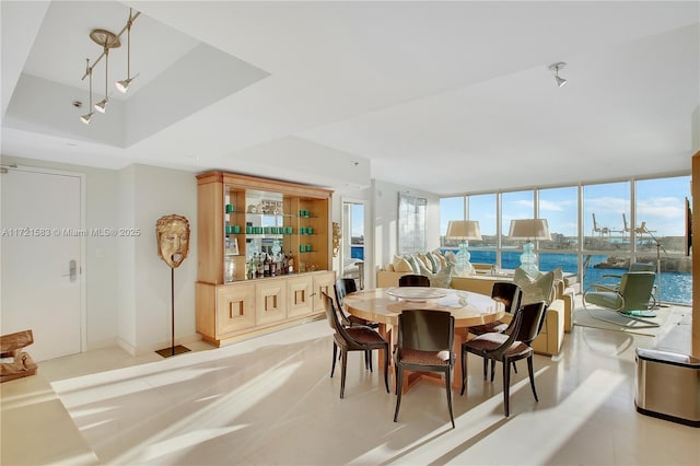 dining space with a water view, a raised ceiling, and expansive windows