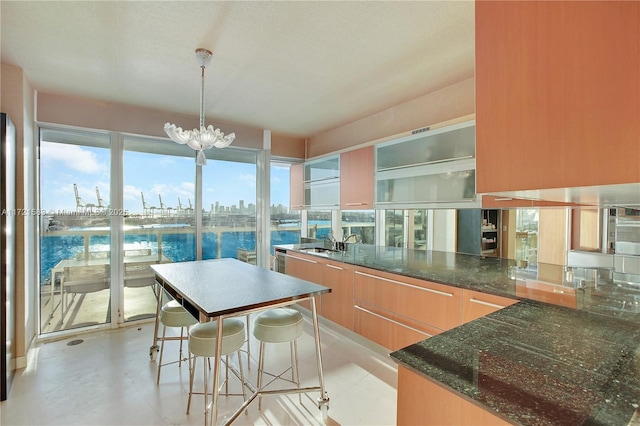 kitchen with a kitchen breakfast bar, dark stone counters, sink, decorative light fixtures, and an inviting chandelier