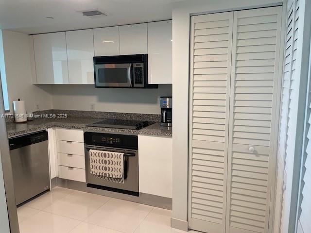 kitchen with dark stone countertops, white cabinetry, stainless steel appliances, and light tile patterned floors