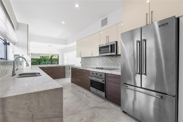 kitchen featuring sink, tasteful backsplash, white cabinetry, dark brown cabinets, and appliances with stainless steel finishes