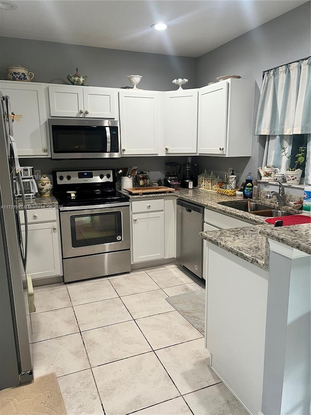 kitchen with sink, white cabinetry, stainless steel appliances, light tile patterned floors, and light stone counters