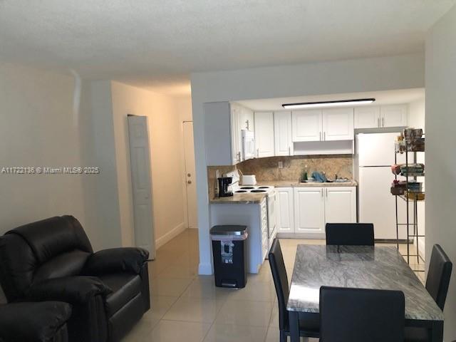 kitchen featuring white cabinets, white appliances, backsplash, and light tile patterned floors