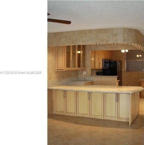 kitchen featuring kitchen peninsula, black fridge, a textured ceiling, ceiling fan, and light tile patterned flooring