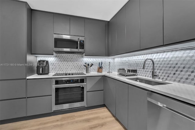 kitchen featuring decorative backsplash, appliances with stainless steel finishes, gray cabinetry, sink, and light hardwood / wood-style floors