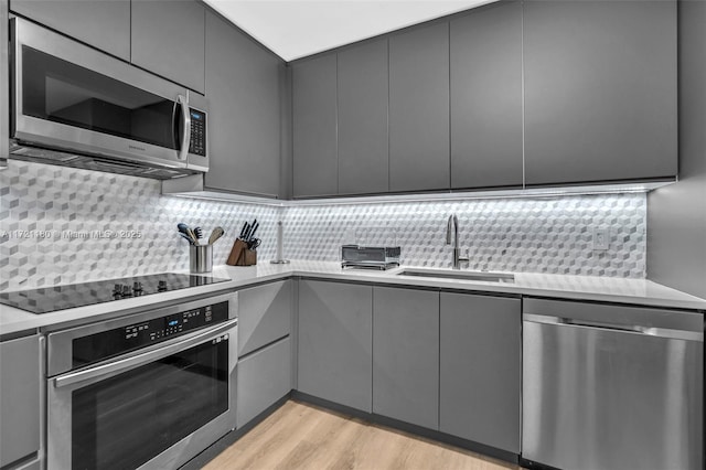 kitchen with sink, stainless steel appliances, tasteful backsplash, light hardwood / wood-style flooring, and gray cabinets