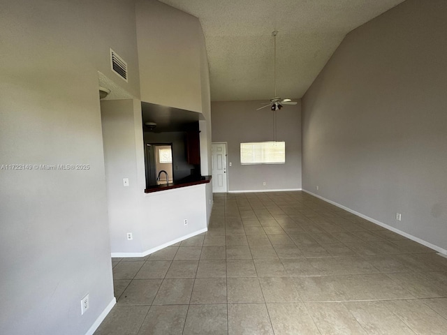 spare room with a high ceiling, a textured ceiling, tile patterned floors, and ceiling fan