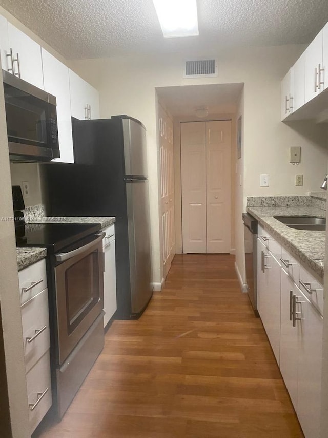 kitchen featuring a textured ceiling, stainless steel appliances, sink, hardwood / wood-style flooring, and white cabinets