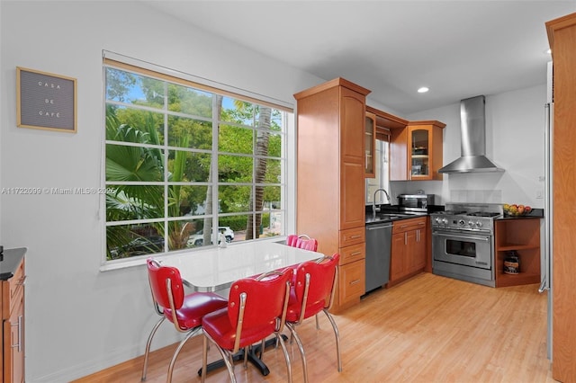 kitchen with light wood-type flooring, stainless steel appliances, wall chimney exhaust hood, and sink