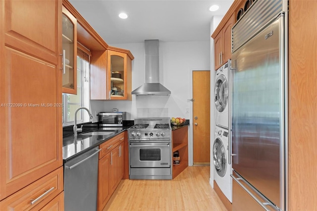 kitchen featuring wall chimney exhaust hood, sink, light hardwood / wood-style flooring, stacked washer and clothes dryer, and high quality appliances