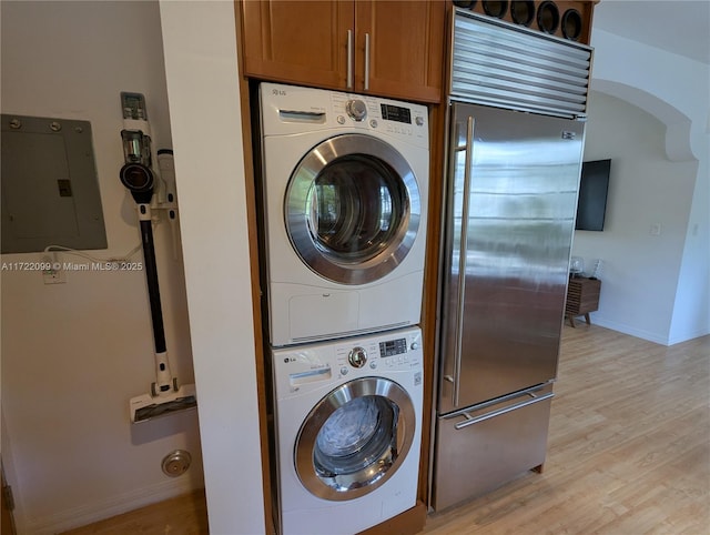 laundry room featuring electric panel, stacked washer and dryer, and light hardwood / wood-style flooring