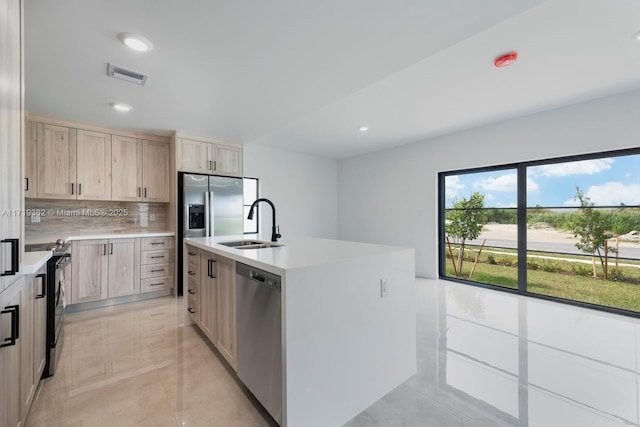 kitchen with sink, stainless steel dishwasher, decorative backsplash, light brown cabinetry, and a center island with sink