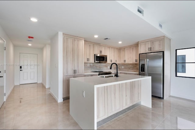 kitchen featuring sink, stainless steel appliances, light brown cabinetry, light tile patterned floors, and a center island with sink