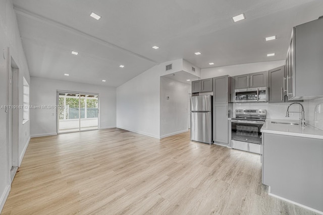 kitchen featuring gray cabinetry, sink, vaulted ceiling, light wood-type flooring, and stainless steel appliances