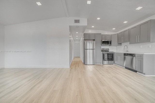 kitchen with gray cabinetry, lofted ceiling, sink, light hardwood / wood-style flooring, and stainless steel appliances