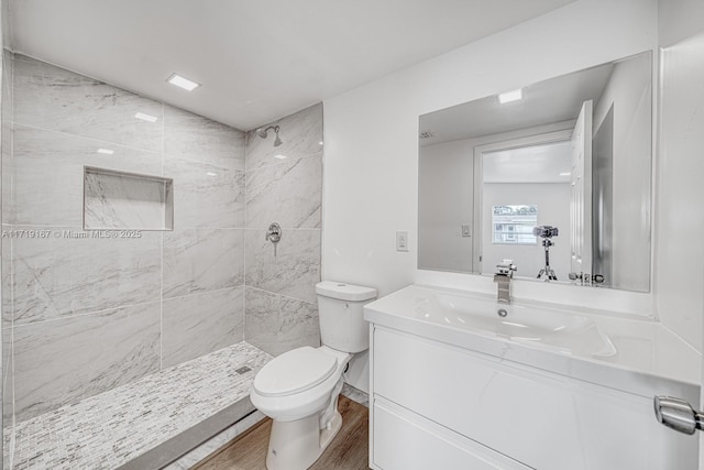 bathroom with hardwood / wood-style flooring, toilet, vanity, and tiled shower