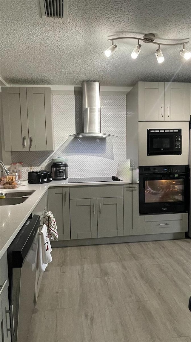 kitchen featuring black appliances, a textured ceiling, sink, light hardwood / wood-style flooring, and wall chimney exhaust hood