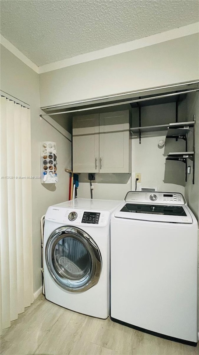 clothes washing area with light hardwood / wood-style floors, a textured ceiling, cabinets, and separate washer and dryer