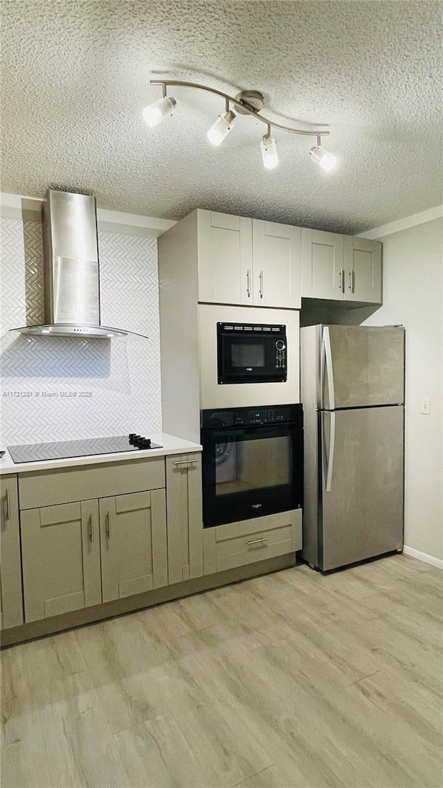 kitchen featuring wall chimney exhaust hood, black appliances, light hardwood / wood-style flooring, and a textured ceiling