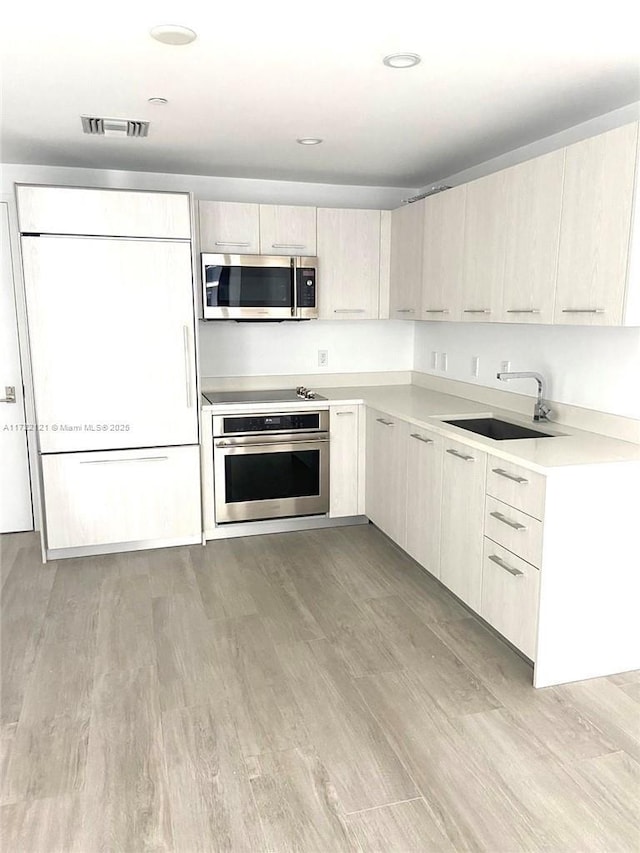 kitchen with appliances with stainless steel finishes, light hardwood / wood-style flooring, and sink