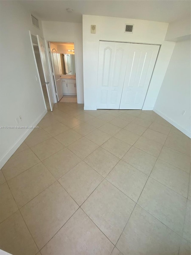 unfurnished bedroom with ensuite bathroom, light tile patterned floors, and a closet