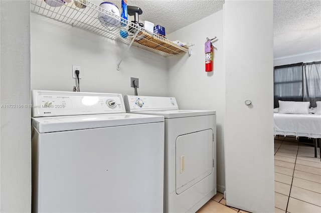 laundry area featuring independent washer and dryer, light tile patterned floors, and a textured ceiling