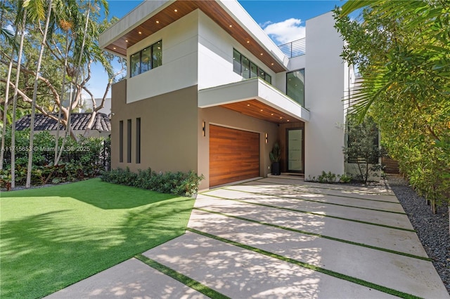 view of front facade with an attached garage, a balcony, concrete driveway, stucco siding, and a front lawn