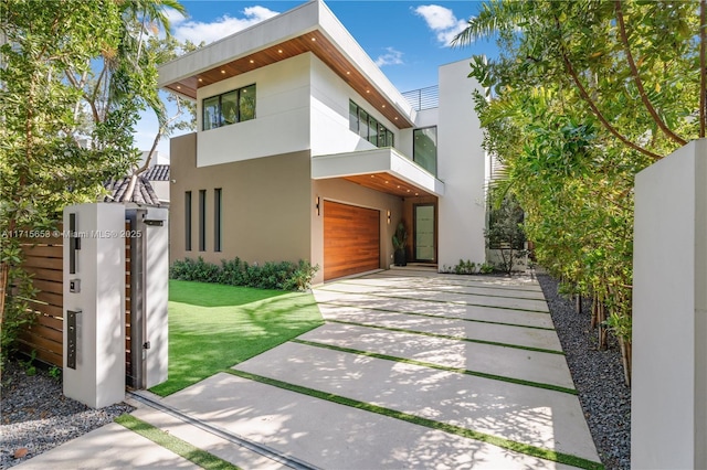 modern home featuring driveway, a garage, a balcony, fence, and stucco siding