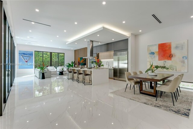 kitchen featuring built in refrigerator, a kitchen breakfast bar, gray cabinets, modern cabinets, and island exhaust hood