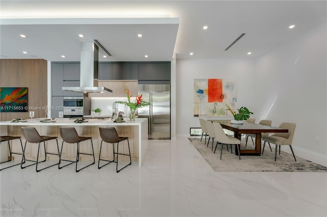 kitchen featuring modern cabinets, a breakfast bar area, island exhaust hood, gray cabinets, and built in fridge