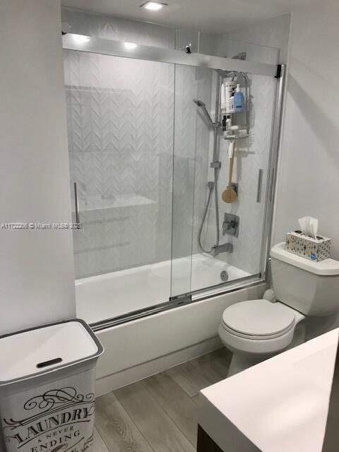 bathroom with hardwood / wood-style floors, toilet, and enclosed tub / shower combo