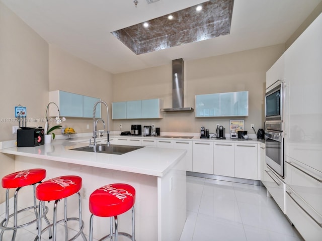 kitchen featuring wall chimney exhaust hood, light countertops, stainless steel oven, modern cabinets, and a kitchen breakfast bar