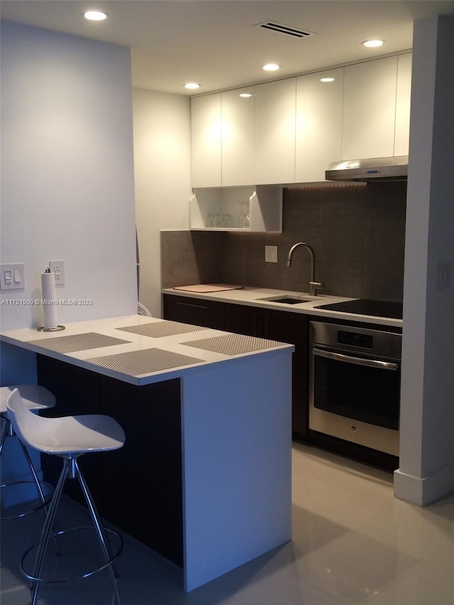 kitchen with a breakfast bar, stainless steel oven, white cabinetry, and sink