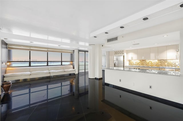 kitchen with stainless steel fridge, backsplash, light stone counters, dark tile patterned floors, and white cabinets