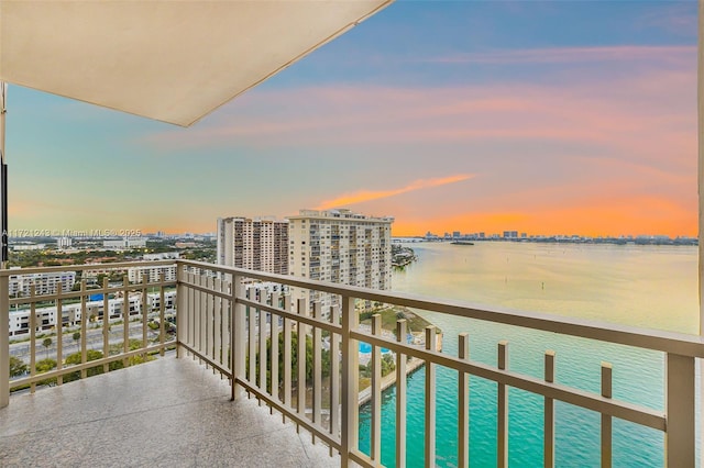 balcony at dusk featuring a water view