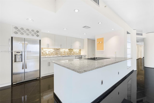 kitchen with light stone counters, backsplash, built in refrigerator, black electric stovetop, and white cabinets