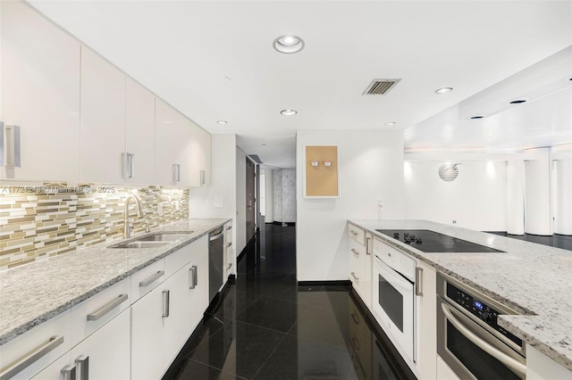 kitchen with white cabinets, appliances with stainless steel finishes, light stone counters, and sink