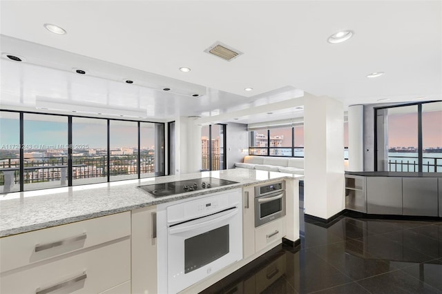 kitchen featuring white oven, black electric stovetop, oven, light stone counters, and white cabinetry