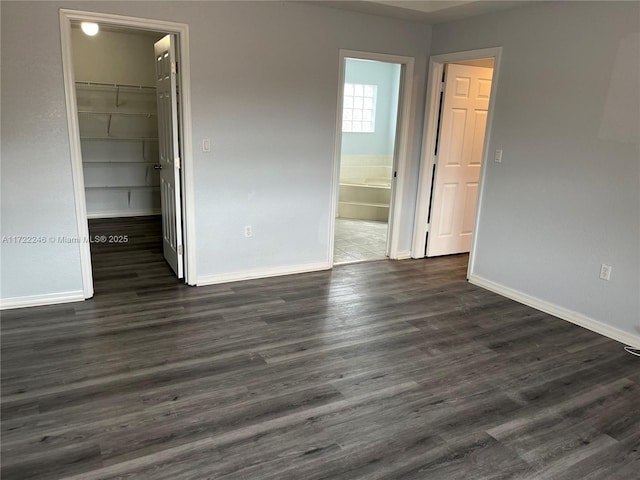 unfurnished bedroom with a walk in closet, a closet, ensuite bath, and dark hardwood / wood-style floors